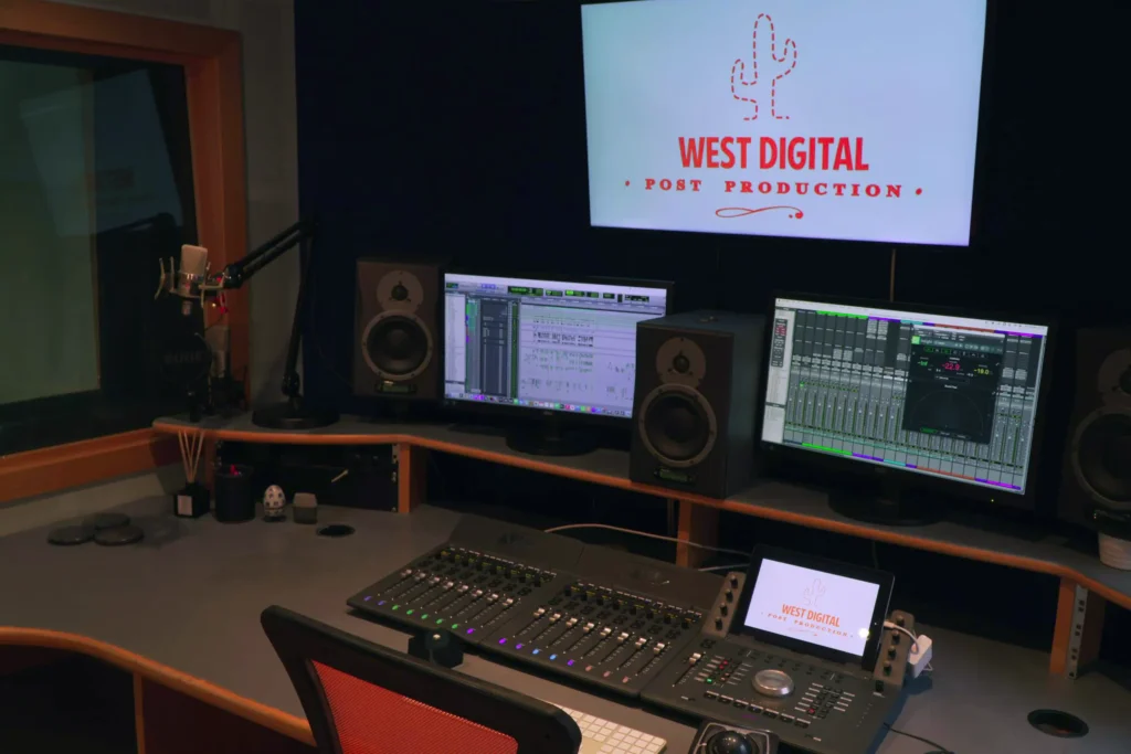 The audio suite control room, with the voiceover booth visible through the glass