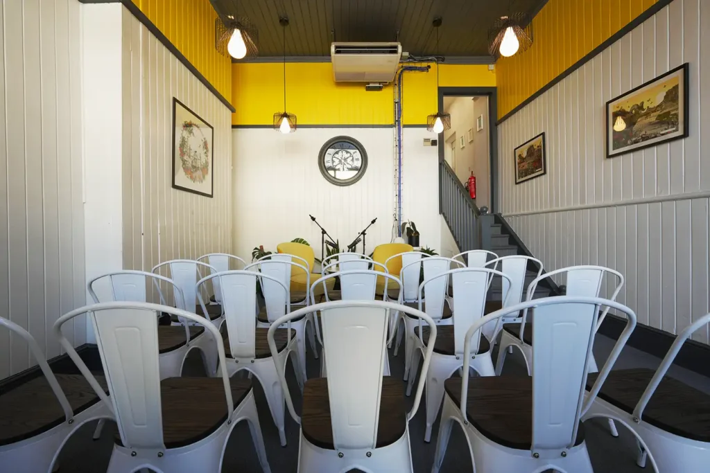 Event space laid out theatre-style, white chairs facing two yellow armchairs and microphone stands