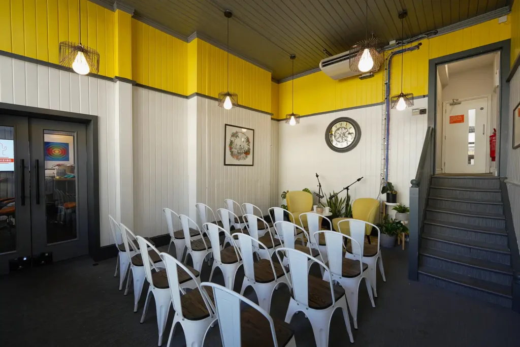 Ground-floor event space set for an audience, with a staircase and glazed doors through to the studio
