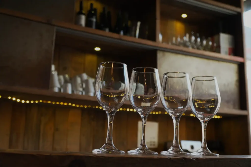 Wine glasses on the bar, with bottles and glassware on the shelves behind