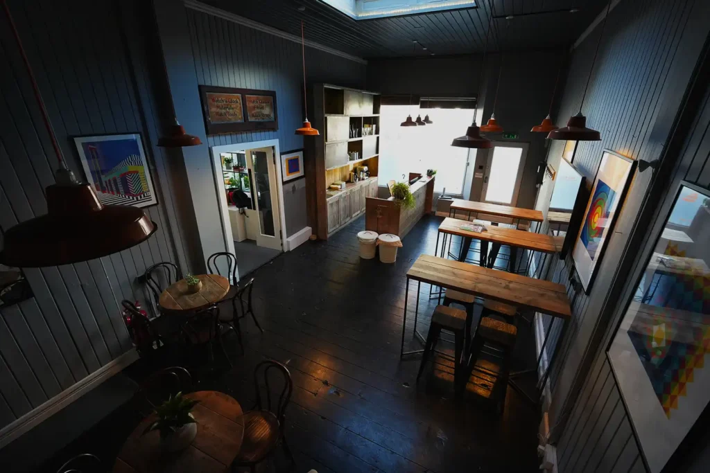 Cafe bar with a serving counter, high tables and framed prints under a skylight