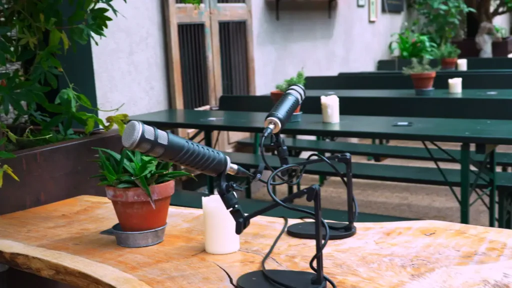 Two broadcast microphones set up on a wooden table in a courtyard for a mobile podcast recording