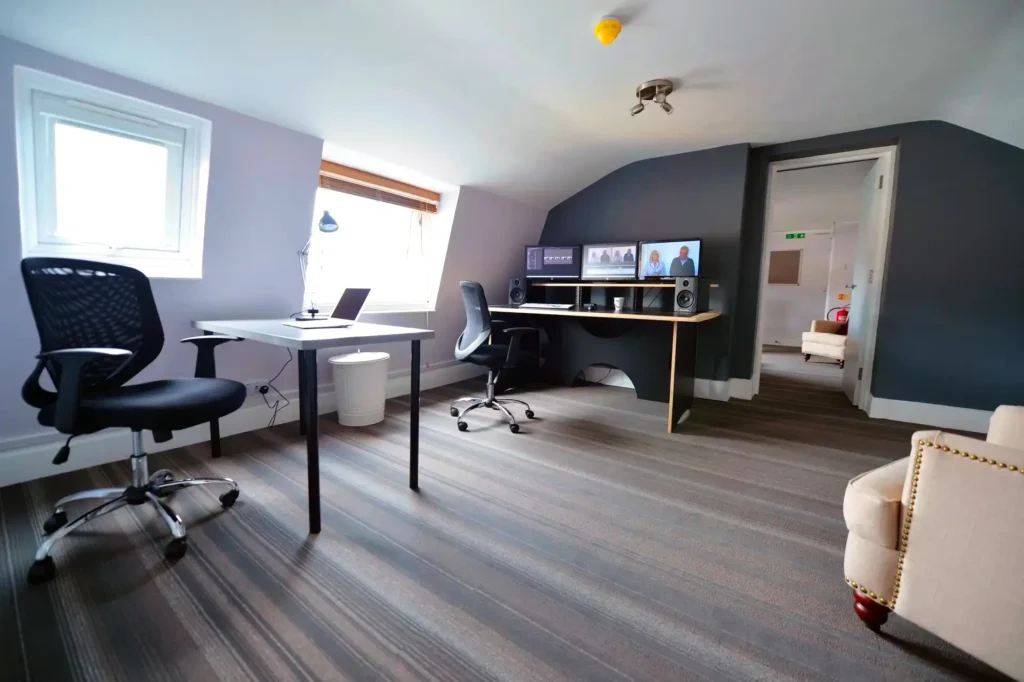Edit suite with a two-monitor edit desk, studio speakers and a spare meeting table under the window